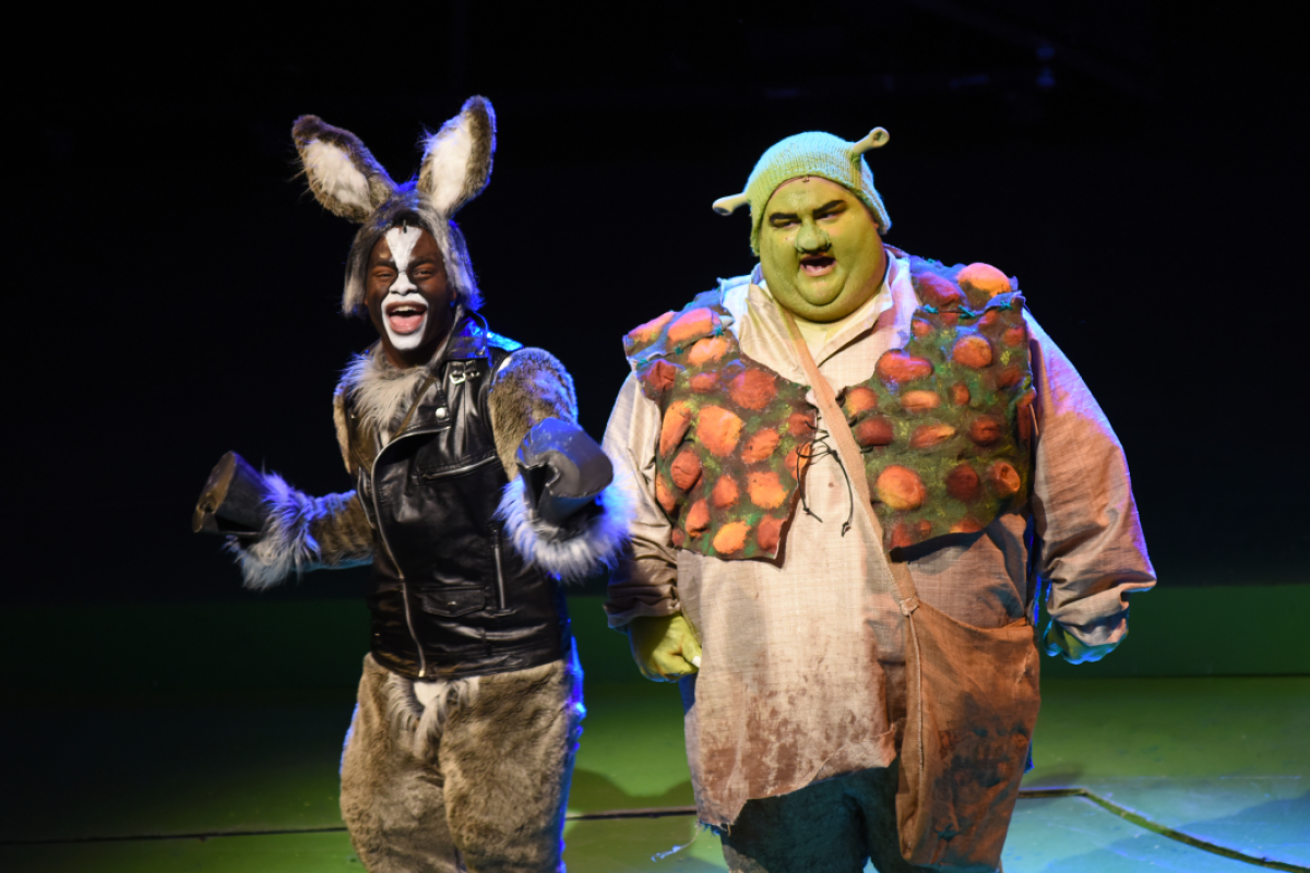 Two performers dressed as Shrek and Donkey perform on stage.