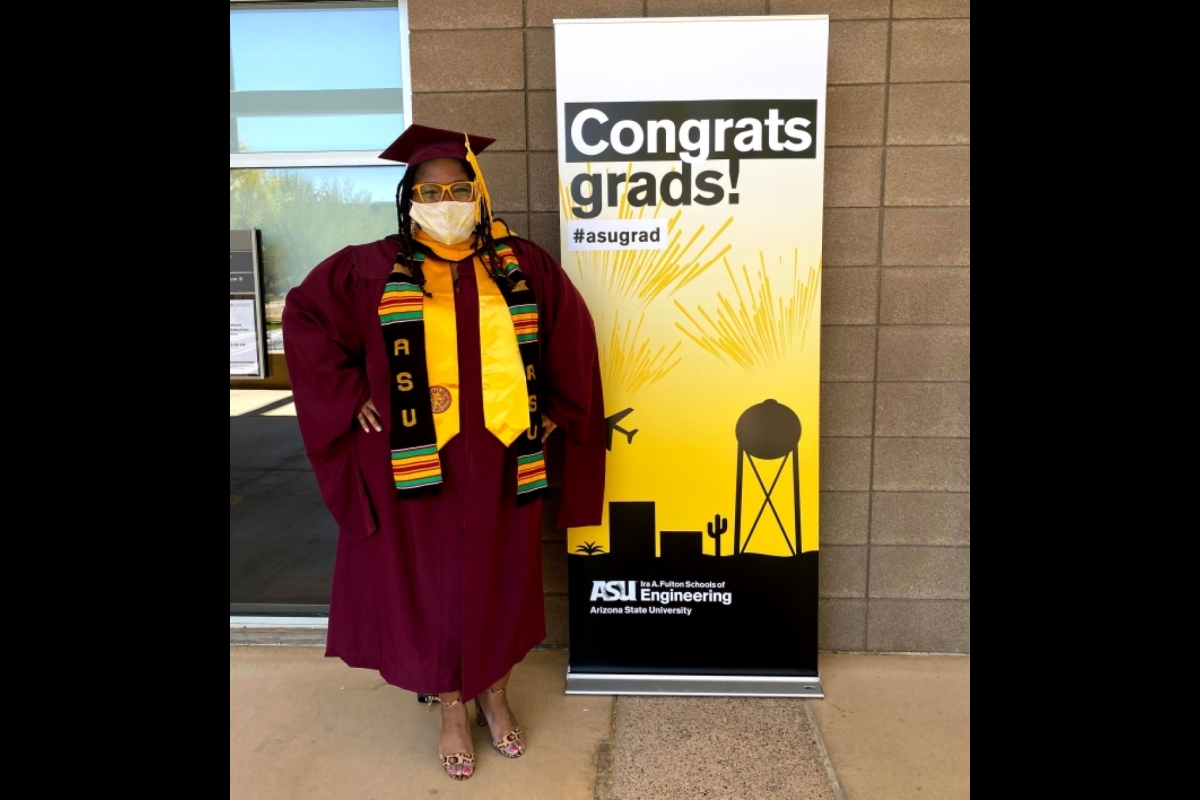 A woman in graduation robes poses in front of a sign that says Congrats, grads!