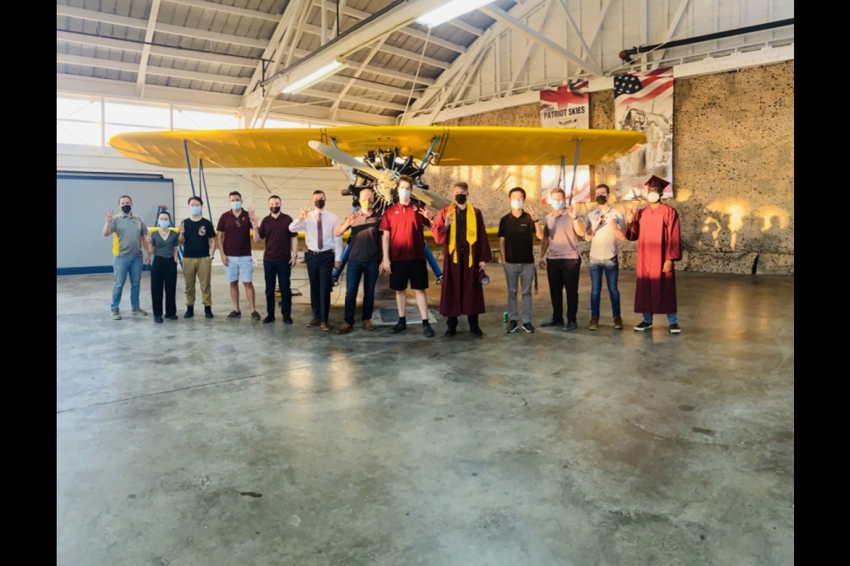 Students line up in front of an old prop plane inside a hangar