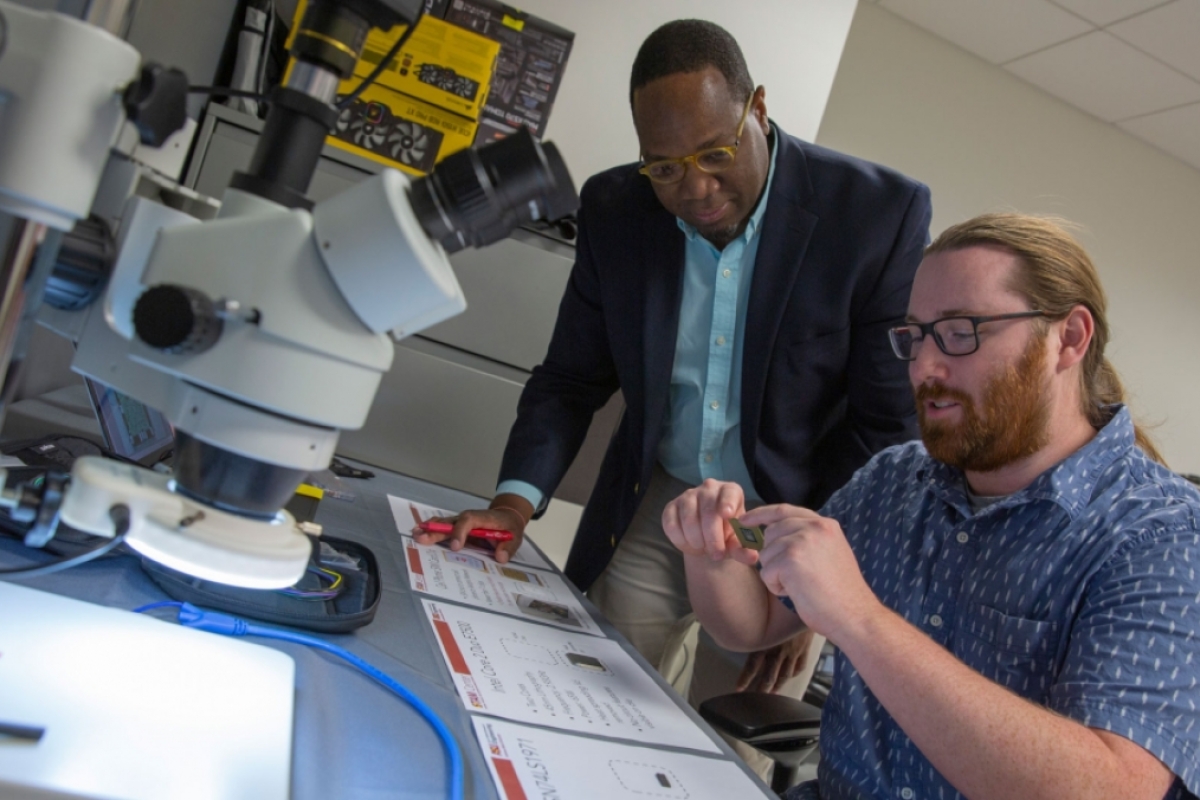 Michel Kinsy leans over to inspect a semiconductor in the hands of Graduate Research Associate Alan Ehret in the STAM Center at ASU.