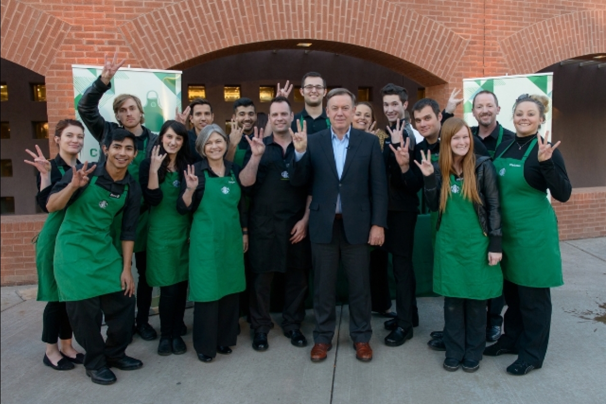 ASU President Michael Crow standing with a group of people wearing green aprons and making the ASU pitchfork symbol with their hands.