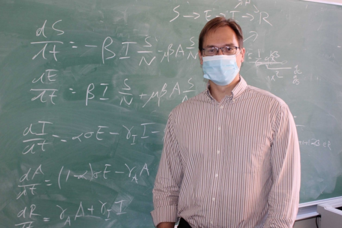Steffen Eikenberry stands in front of a chalkboard with equations written on it