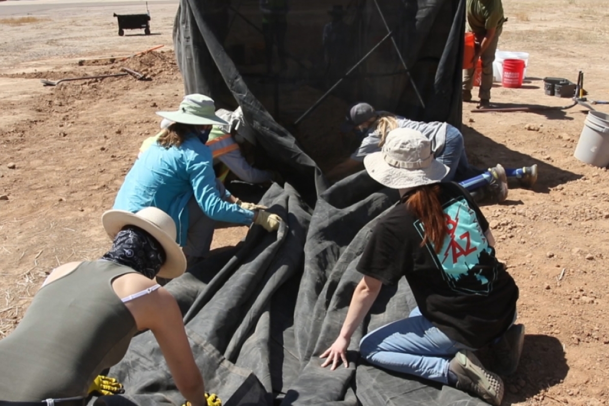 Five volunteers kneel preparing to roll up excess shade cloth