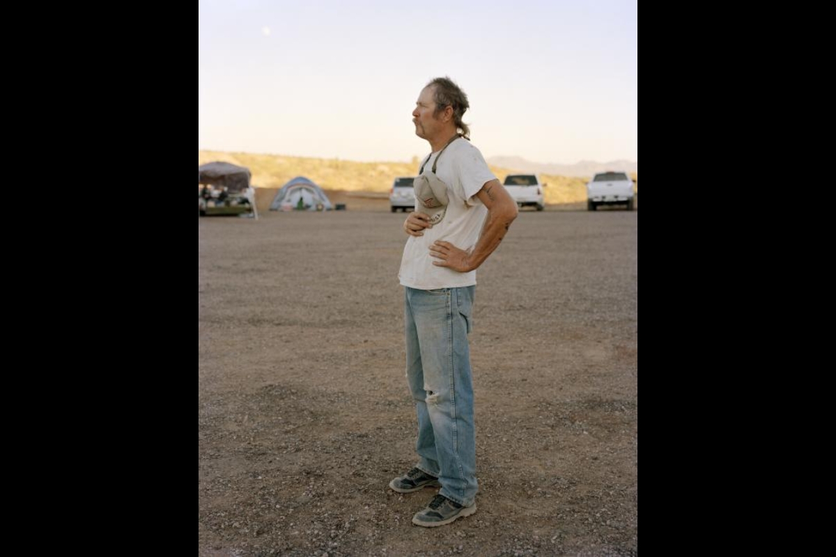 Photo by Pam Golden shows a white man with a ponytail, wearing faded jeans and a t-shirt, standing in profile with his hands on his hips.