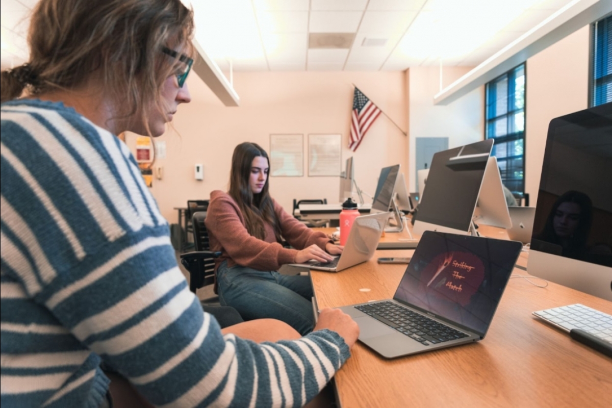 Two students work on their laptops, one displaying a poster design.