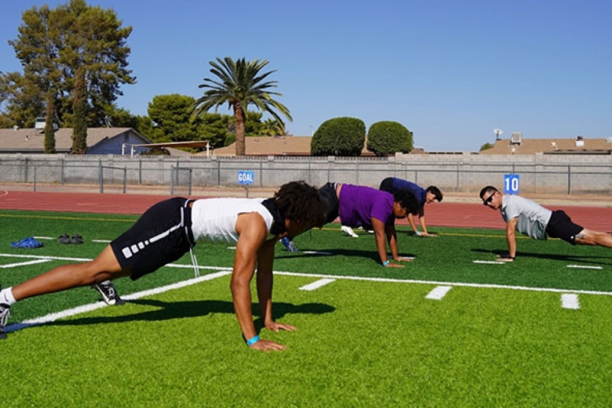 High school athletes doing pushups on a field.