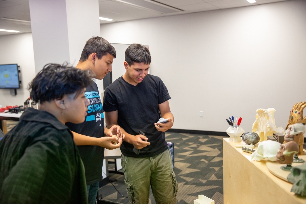 Three high school students look at 3D-printed objects.
