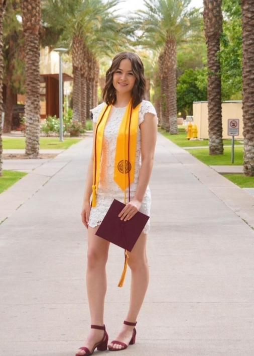 ASU's College of Health Solutions graduate Emma Utagawa smiles while holding her graduation cap on Palm Walk at ASU's Tempe campus