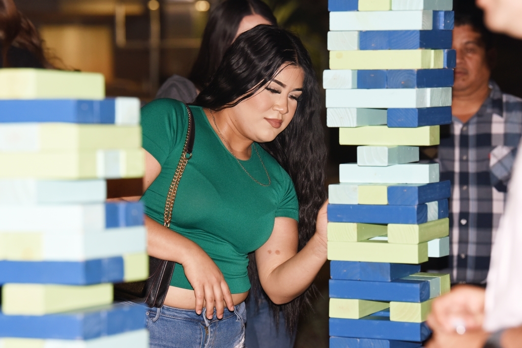 Woman removing a block from a large tower of wooden blocks.