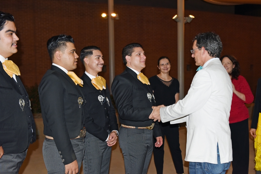 Man wearing a white suit jacket shaking the hands of mariachi band members.