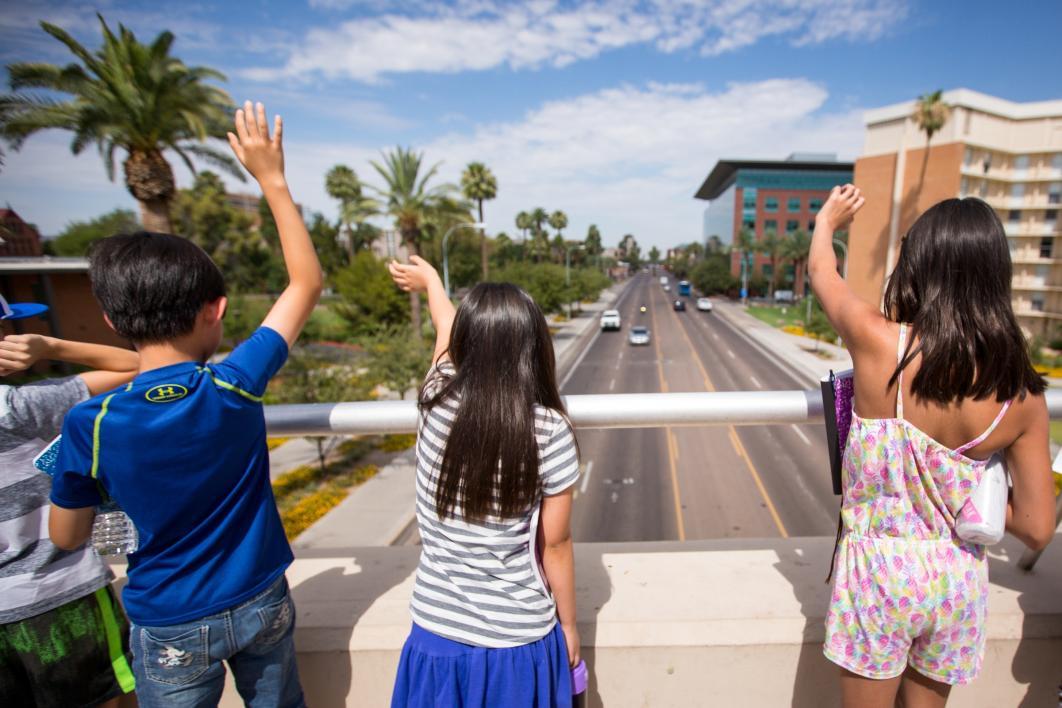 Students wave at traffic while standing on the University Drive bridge during Young Adult Writing Program