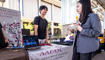 Student standing behind a table at the visiting booth speaking to another student with a popsicle at ASU's Culture Kickoff event.