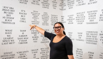 Woman pointing to a wall with various phrases printed on it.