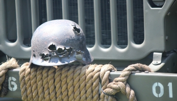 Close-up image of the front of a battered helmet resting on the front bumper of a Jeep.