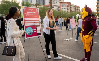 ASU students stand next to a research poster while talking to Sparky the Sun Devil mascot.