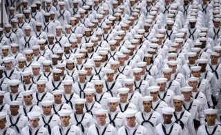 Several neat rows of people dressed in white U.S. Navy regalia.
