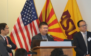 Person standing at a podium with other people surrounding them and U.S., Arizona and ASU flags behind them.