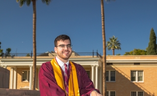 Chris Green in graduation robes sitting on steps at the Tempe campus