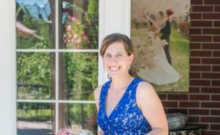 Smiling woman wearing a blue dress and holding a bouquet of flowers.