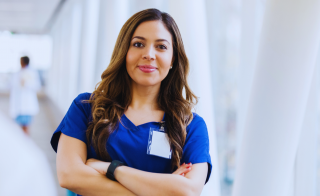A nurse in blue scrubs poses with her arms crossed.