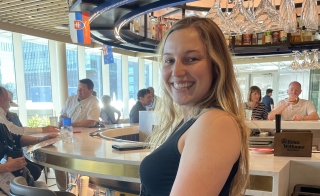 Julie Schuldt sitting on a stool at a round bar, looking over her shoulder and smiling.