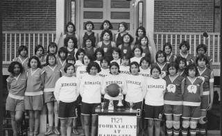 Black-and-white photo of a group of Native American students posed for an athletics photo on a staircase at a school.