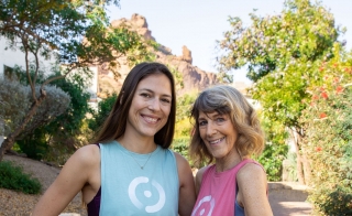 ASU alum Sophie Aigner and her mother, Vickie, pose for a photo on a brick walkway surrounded by greenery and a mountain formation in the background.