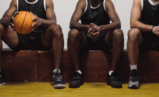 Three men of different ethnicities wearing sports jerseys sitting on a bench. One holds a basketball.