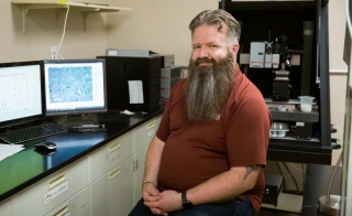 ASU Assistant Professor Christian Hoover sits in his lab in front of a computer and lab equipment.