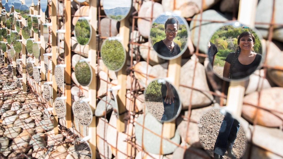 two people reflected in circular mirrors as part of a desert installation
