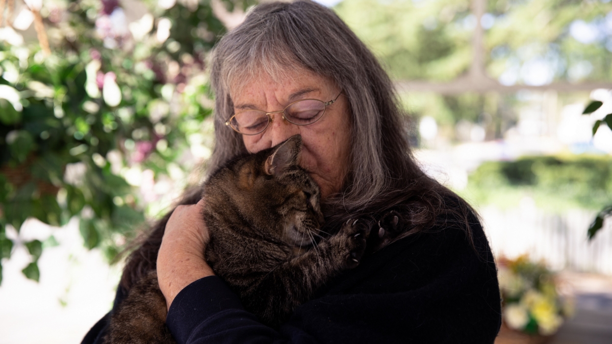 Meals on Wheels client holds her cat close and kisses its head.
