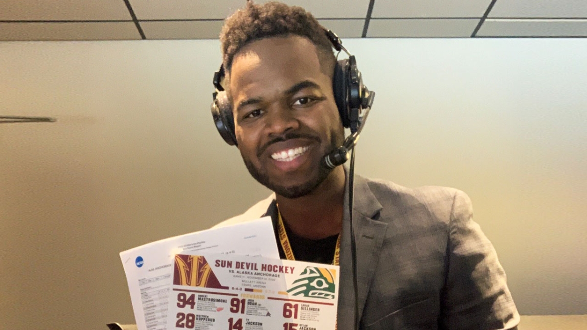 Trey Matthews smiling at the camera holding papers and wearing headphones.