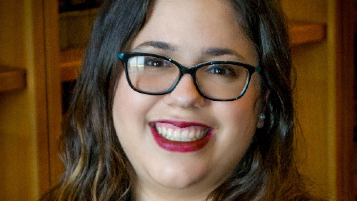 Headshot of Christina Grey in glasses and a black blouse smiling at the camera.