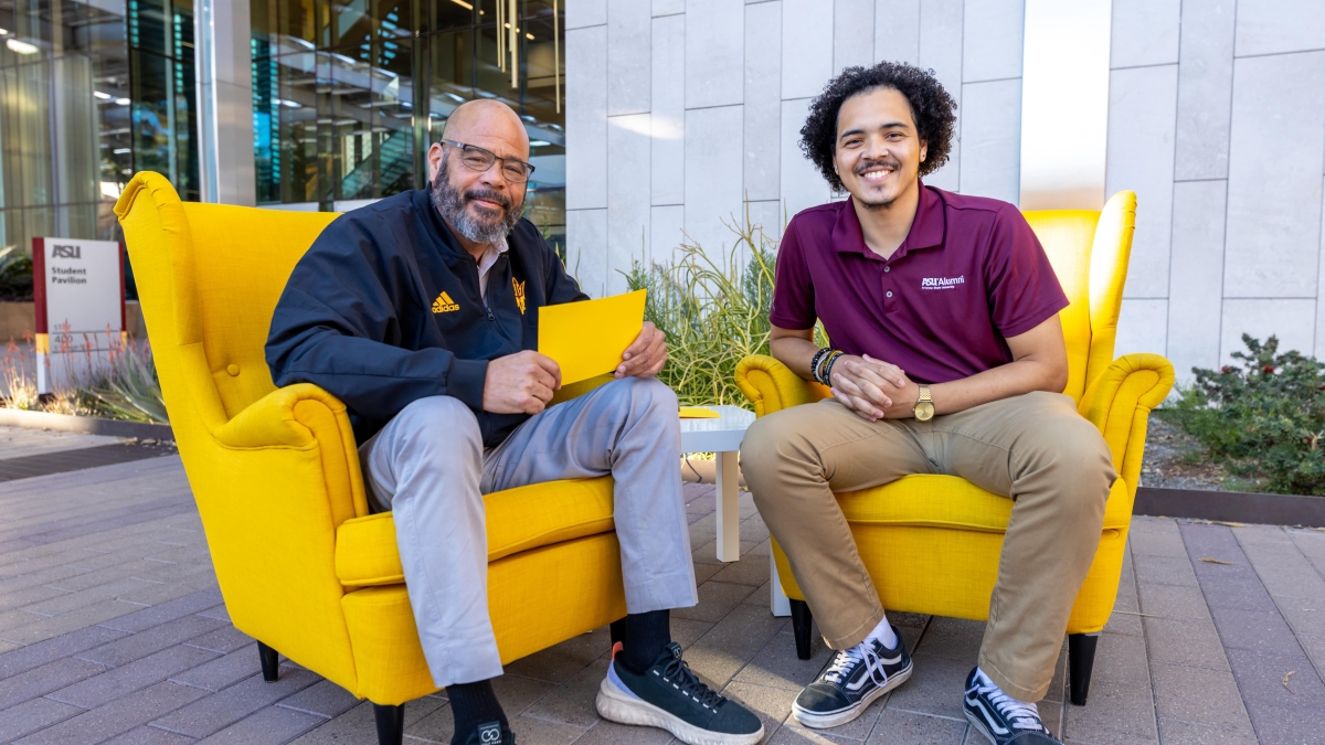 Father and son duo Alonzo and Ahlias Jones smiling while seated in yellow wingback chairs in an outdoor setting.