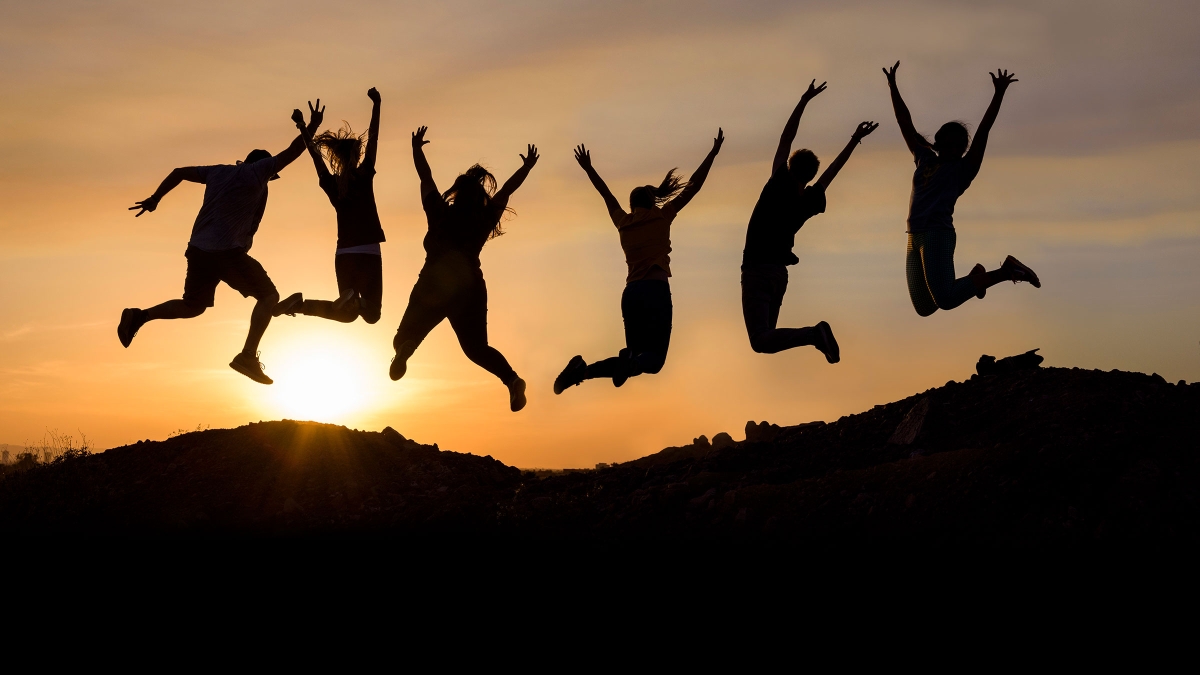Six students jumping are photographed in silhouette against the sunset.