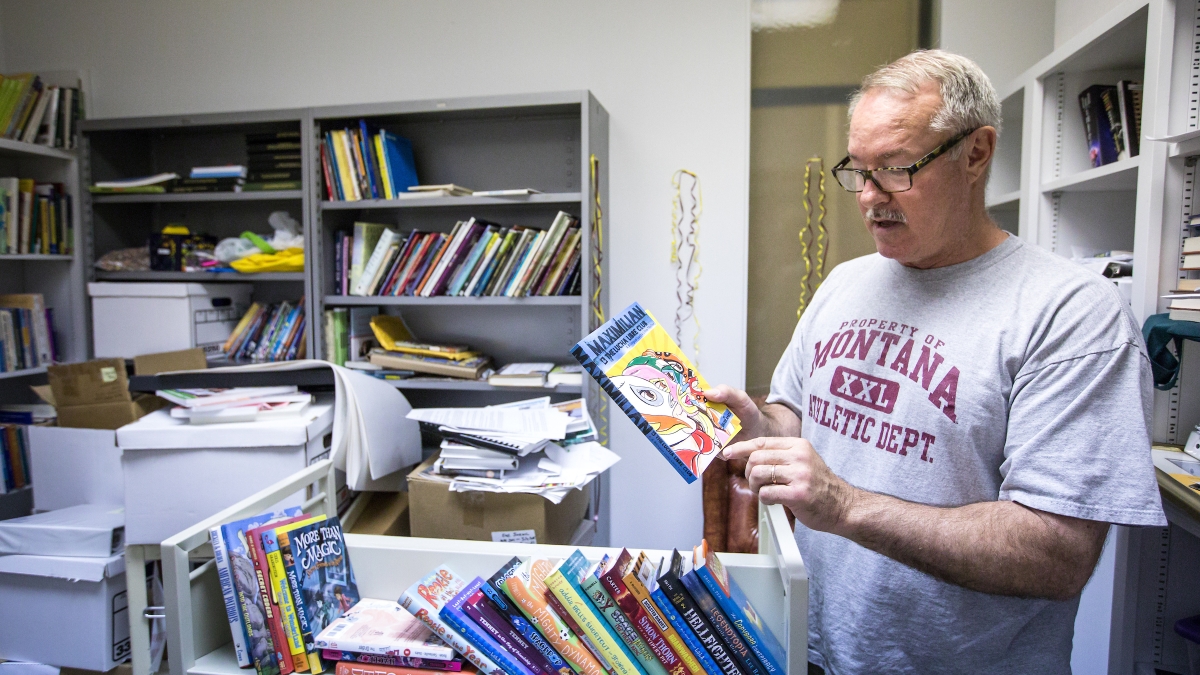 professor holds a book in office full of books 