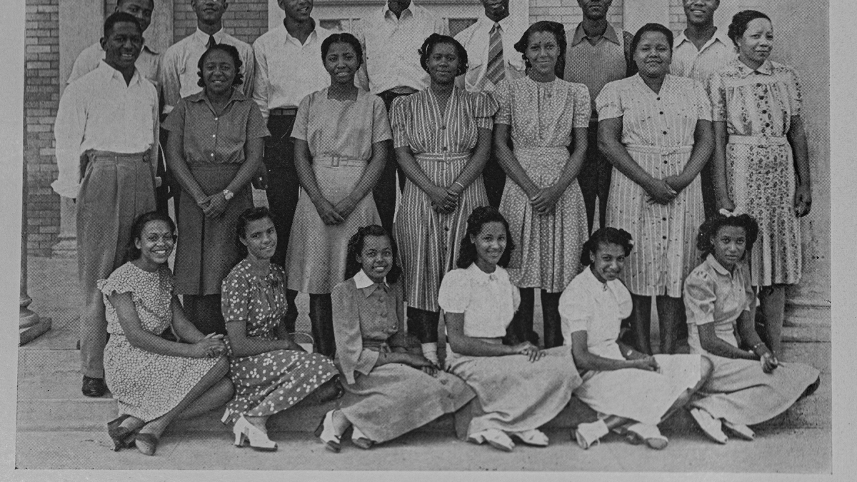 A black and white archival image of a group of pepole standing and sitting posed for the camera