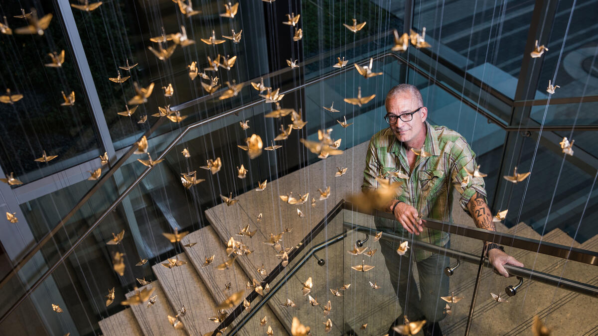 artist posing with art installation of thousands of hanging cranes