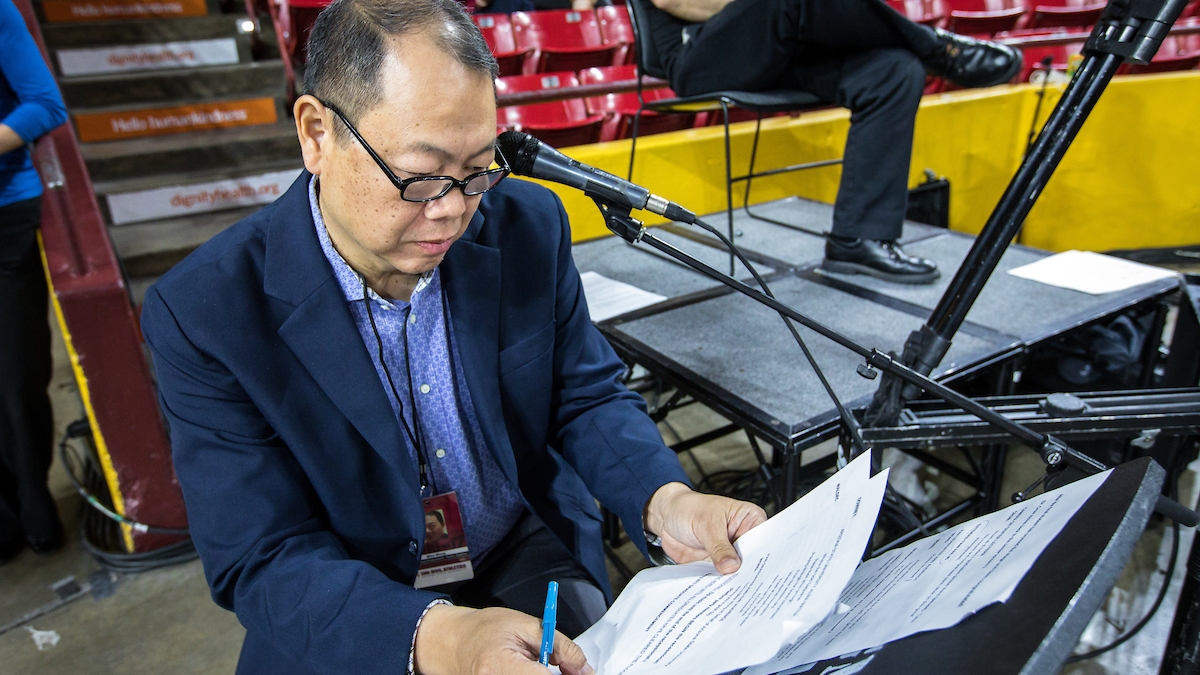Mike Wong seated in front of a microphone in an arena.