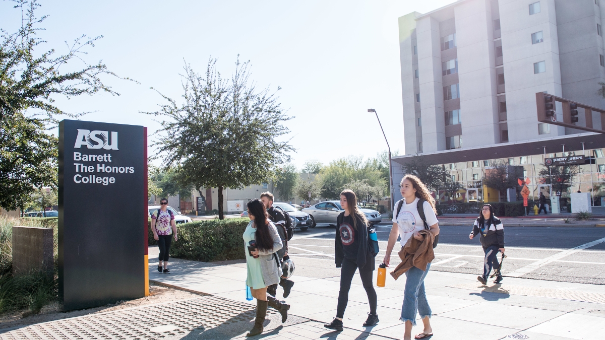 Students walking in front of a sign that reads "ASU Barrett, The Honors College" on ASU's Tempe campus.