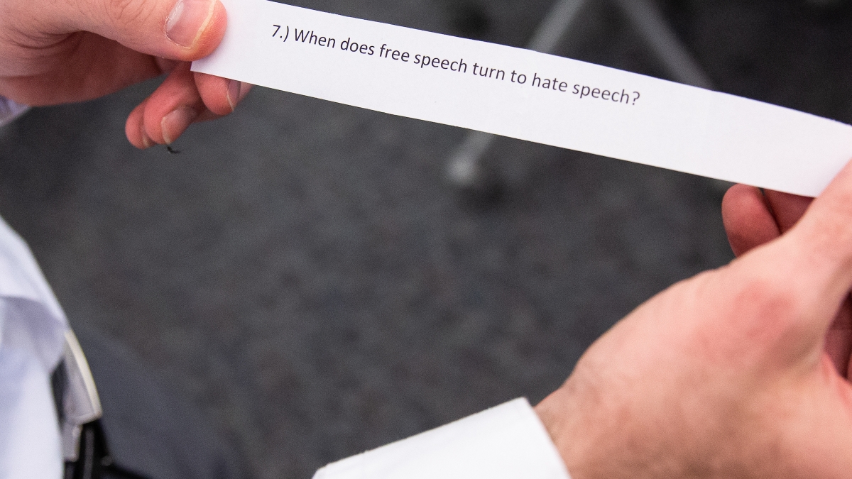 hands holding a piece of paper that reads, "When does free speech turn to hate speech?"