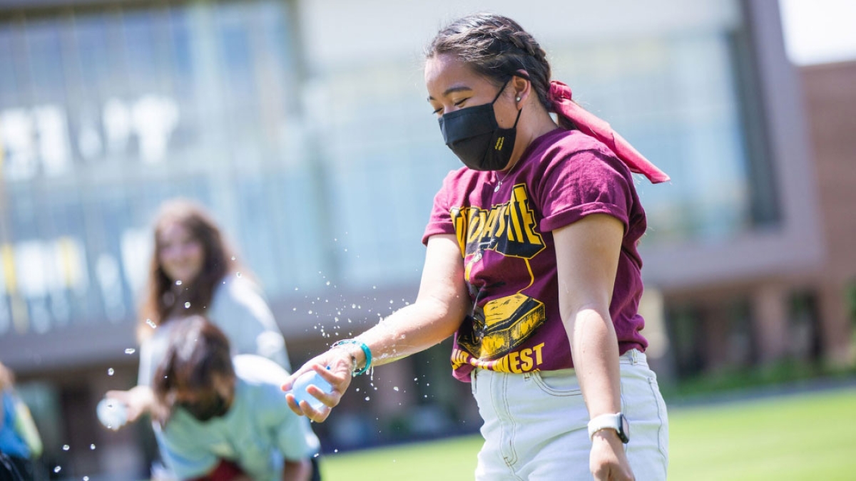 A college student catches a water balloon on a lawn