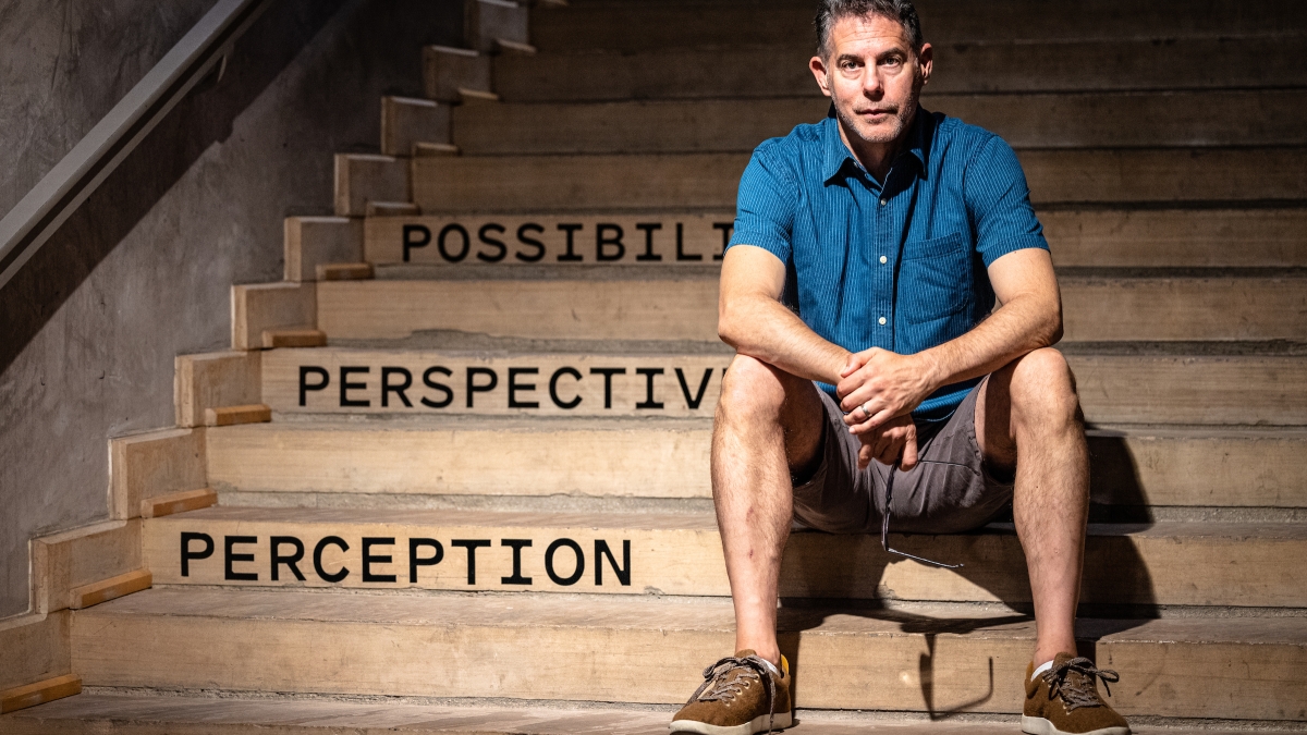 ASU Institute Professor in the School of Music, Dance and Theatre Michael Rohd sits on a stairwell on which the words "possibility," "perspective" and "perception" are written as part of an art installation.