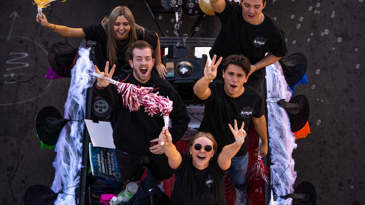 Five members of the ASU undergraduate student government look up from their Homecoming float and cheer at the photographer standing overhead on a bridge