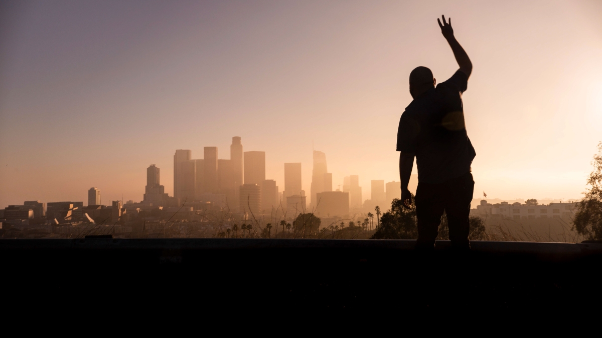 A silhouetted person holds up the ASU pitchfork gesture with the Los Angeles skyline in the background