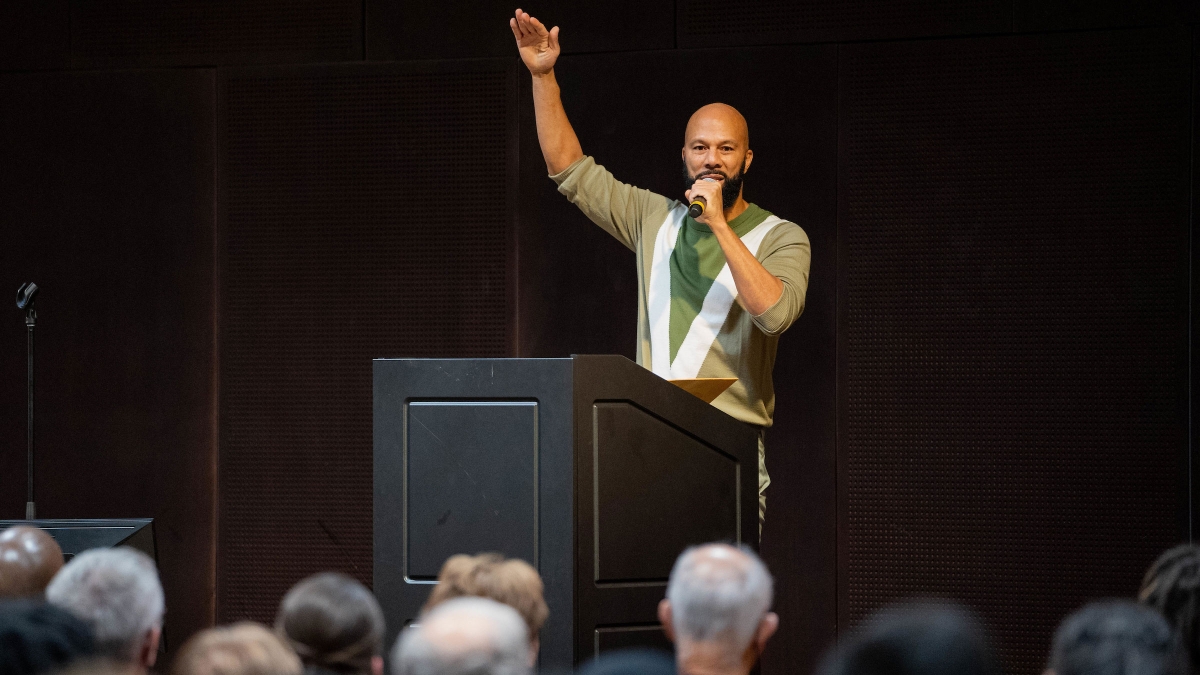 Artist and activist Common gestures while speaking at a lectern in front of a crowd