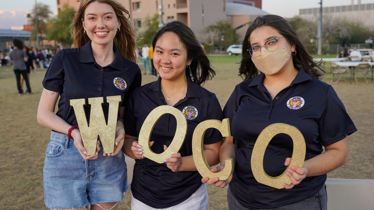 Three women holding gold letters that read "WOCO" at the ASU Women's Coalition Badass Block Party.