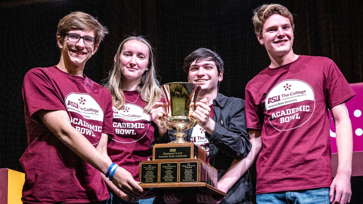 Four college students hold a large trophy after winning the Academic Bowl