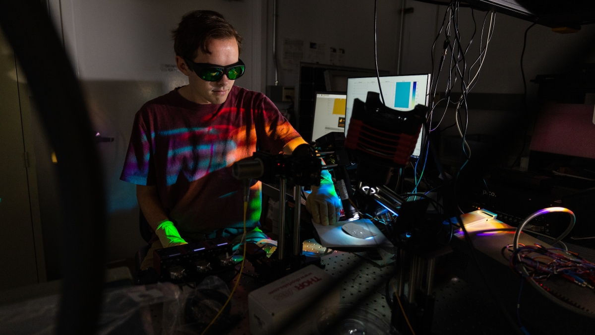 A ma wearing goggles works at a machine with lasers