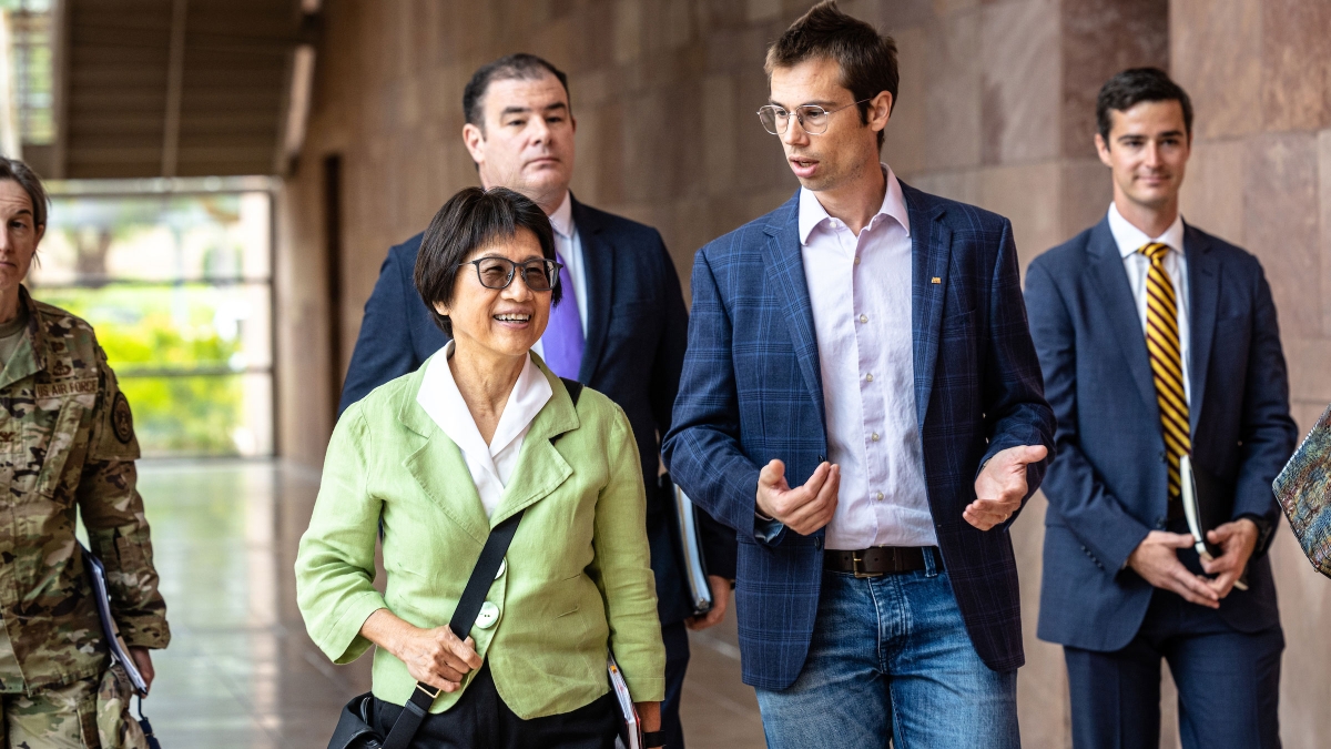 A man and a woman talk while leading a group of people down an outdoor hallway